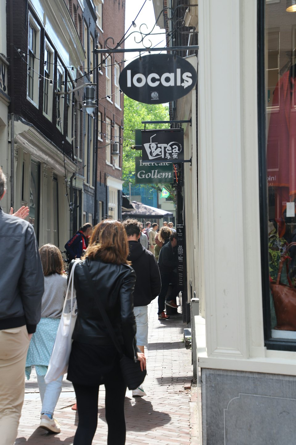 Pedestrians walk down a narrow brick street lined with shops.